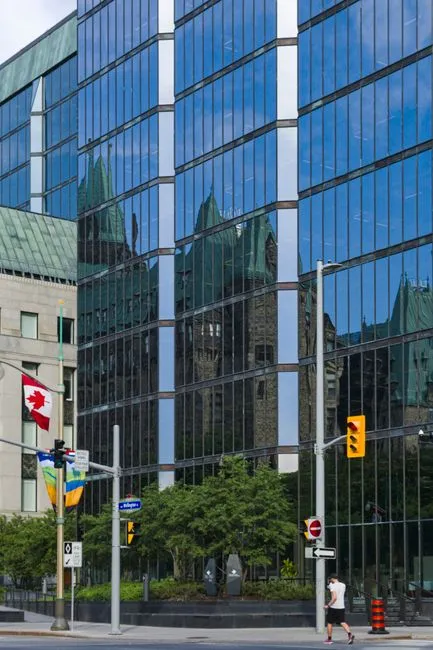 Glass office building in Ottawa reflecting historic architecture with Canadian flags.